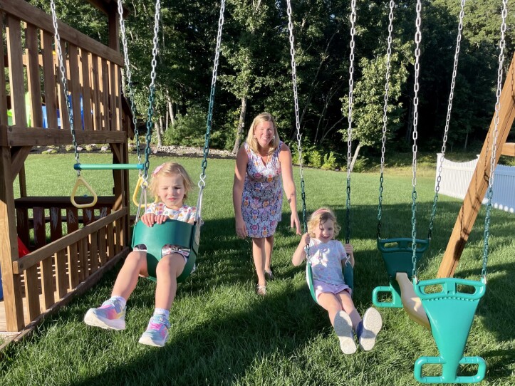 A woman pushed two young girls in swings.