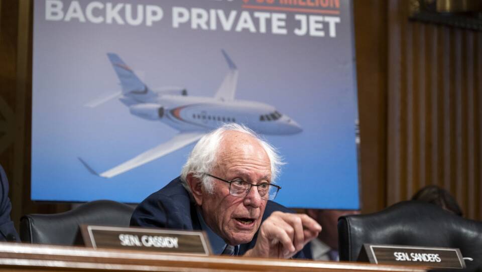 Sanders speaks passionately in front of a poster that shows "Steward Health care's $33 million backup private jet"