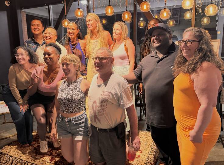 A group of 12 people smile and pose for a photo. Some are kneeling and squatting and others are standing behind and beside those kneeling.