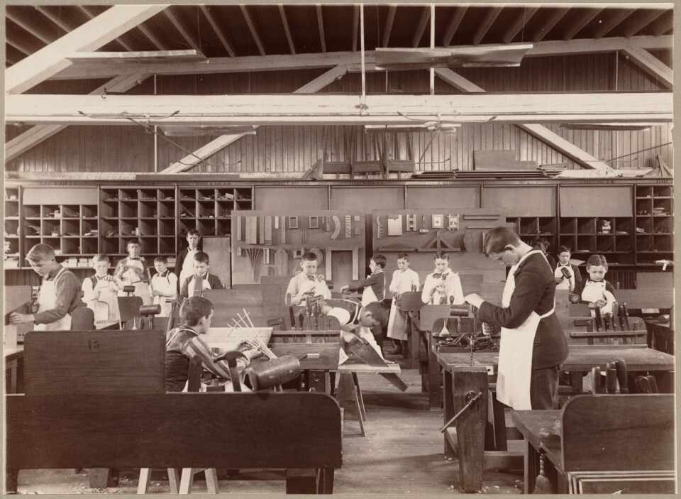 A sepia tone image shows boys in a trade studio making various wood objects.