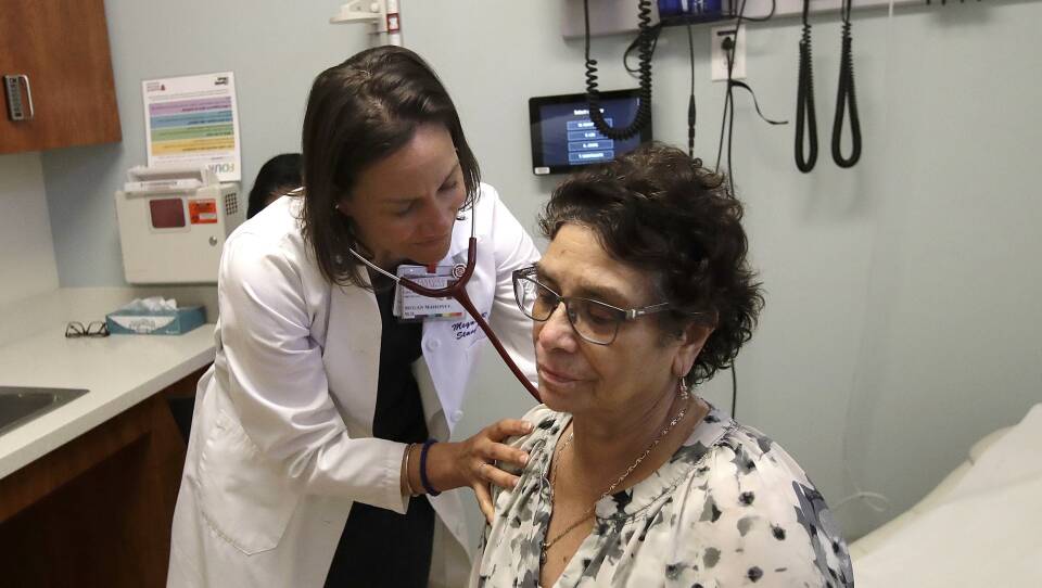 A doctor holds a patient's shoulder as she listens through a stethoscope to their lungs.