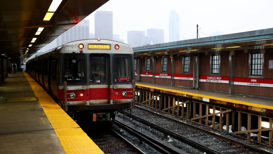A subway train sits on the tracks at an above-ground station on a cloudy day.