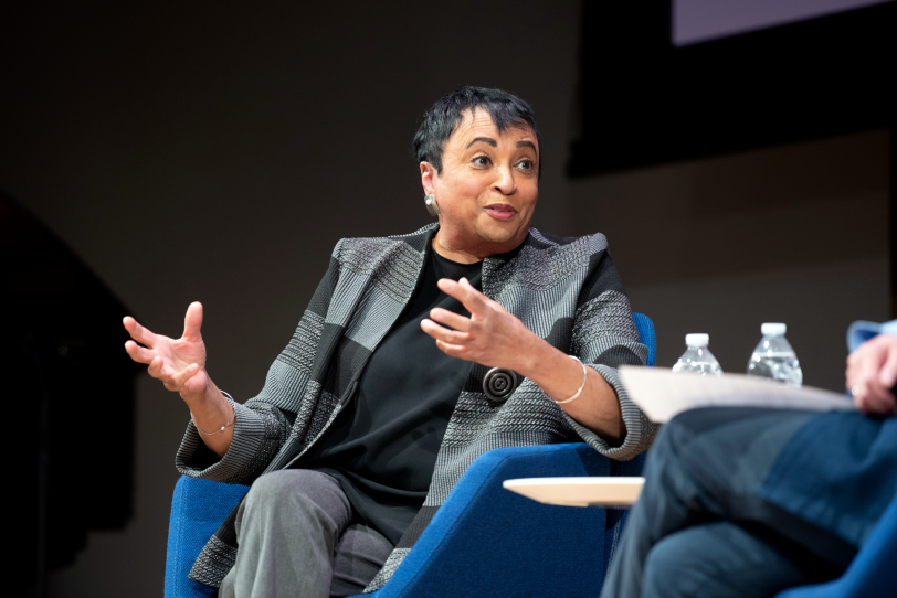 A woman in a blazer speaks on stage in a "fireside chat."