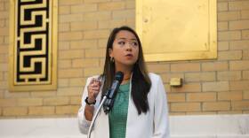A woman in a white blazer speaks at a podium.