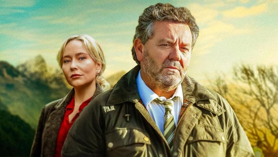 Image of light haired, light skinned woman standing just behind a middle-aged man with a grayish beard and hair