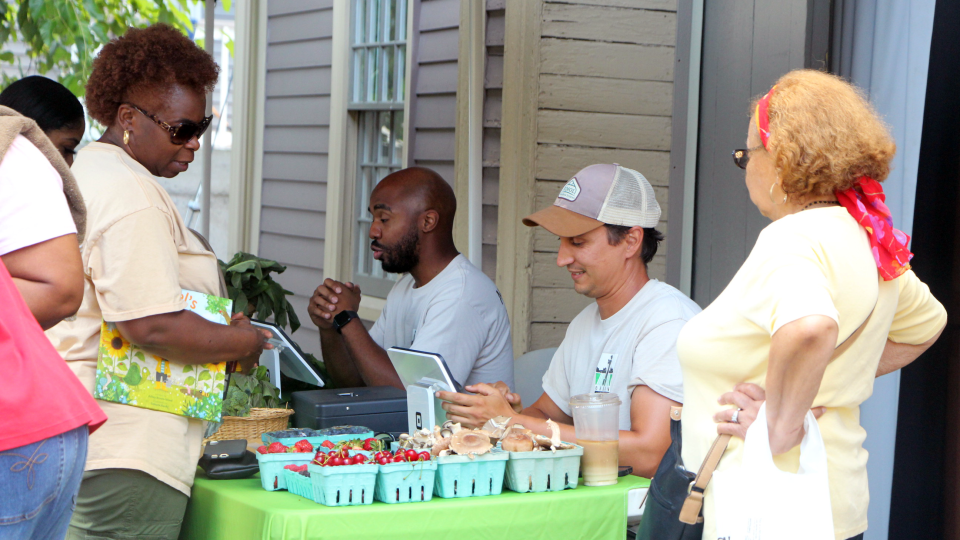 Two people with iPads sell fresh crops outside under a tent.