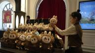A woman arranges a display of furry brown stuffed animals.