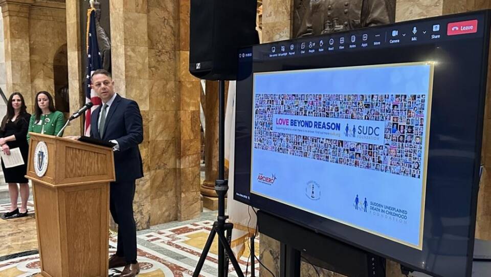 A man in a suit at a lectern, looking toward a screen with the words love beyond reason on it.