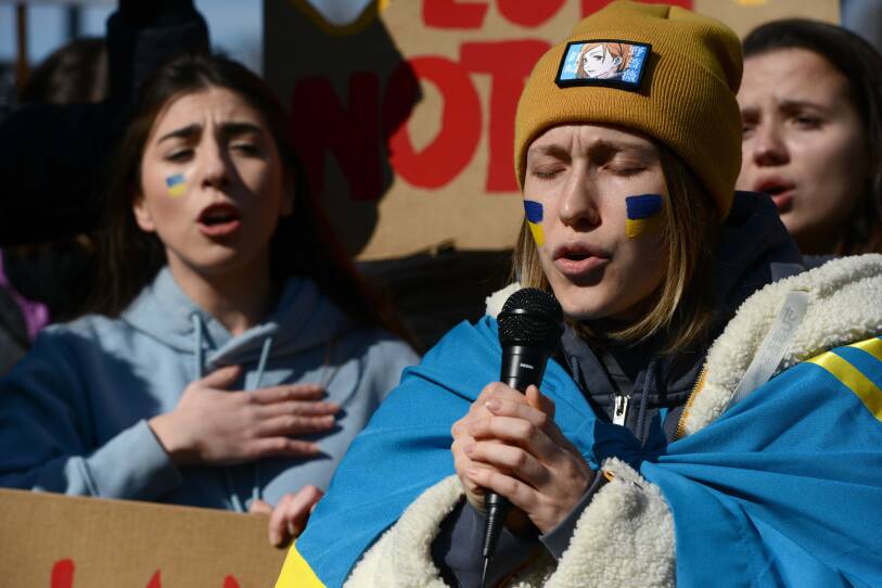 A woman holds a microphone as she and two women behind her sing.