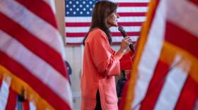 Nikki Haley speaks into a microphone surrounded by American flags at a campaign event in New Hampshire