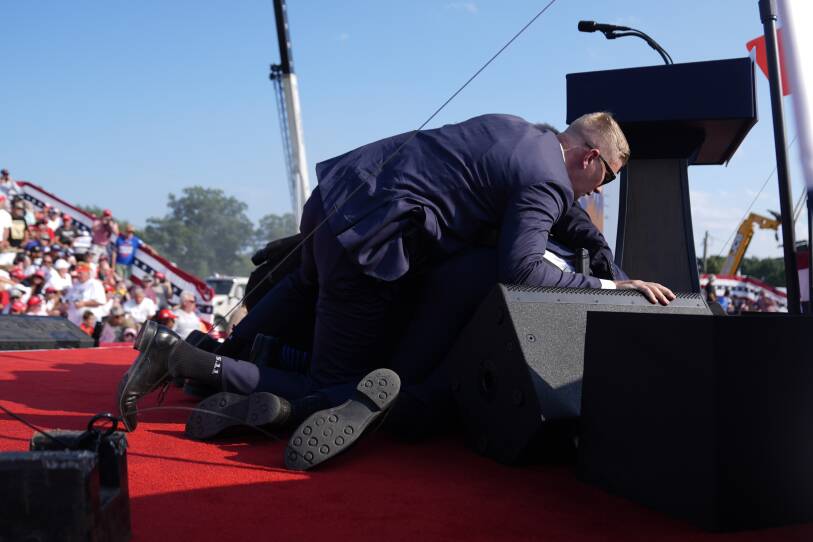 Secret Service agents tackle and cover Donald Trump's body while on stage at a rally.