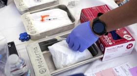 A person places a syringe inside a box labeled Moderna. Boxes with syringes sit next to it.