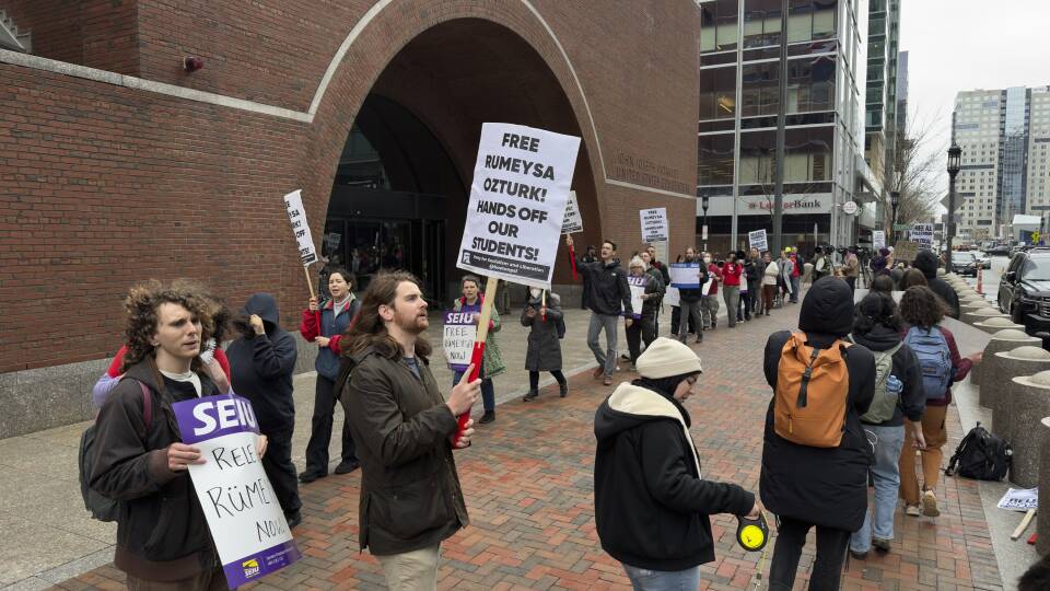 Dozens of people march in a line outside a courthouse, holding signs that say "free Rumeysa Ozturk! Hands off our students!"