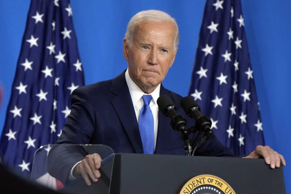 Joe Biden has a serious look on his face while standing behind a podium with the presidential seal.