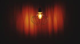 Illuminated Light Bulb Hanging Against Curtain In Dark Theater