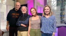 Four people smile for the camera in the Boston Public Library, with the radio program's bright purple set in the background