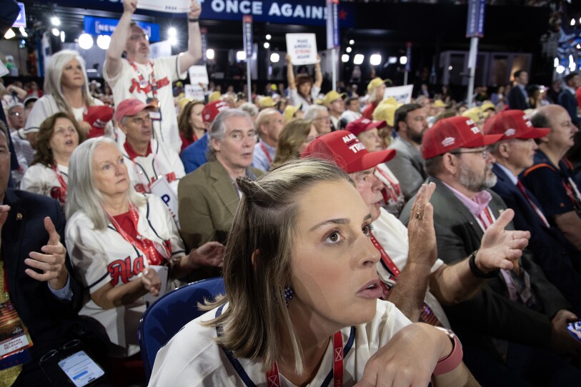 Dozens of people are sitting in an audience at the convention, many wearing pro-Trump hats.