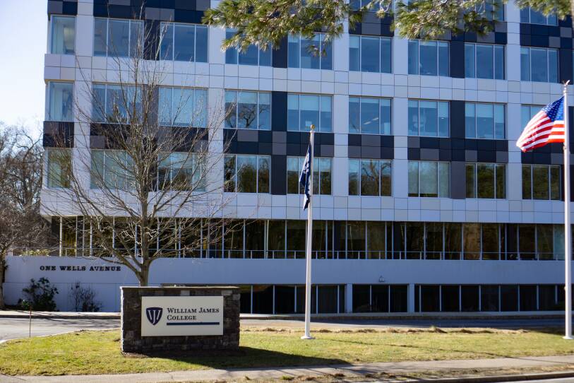A sign reading William James College in front of a large industrial size building.
