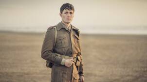 A young man stand in an empty, fallow field, and looks into camera. His hair is greasy and tousled, his face dirty, and he wears a British Soldier's WWII uniform.