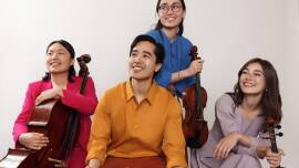 Four people, each holding a string instrument, smiling at the camera