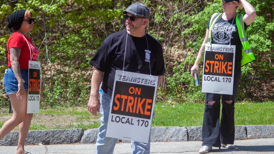 People stand outside with signs that say 'Teamsters Local 170 on strike.'