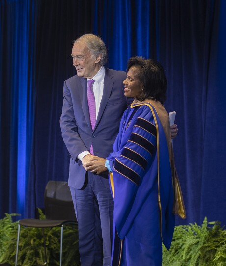 Senator Markey in a suit and newly invested Simmons president in a ceremonial robe clasp hands and smile
