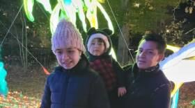 A father with two children are outside wearing jackets. The father is holding one of the children in his arms.