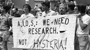 Young men carrying sign that reads: "A.I.D.S: WE NEED RESEARCH, NOT HYSTERIA!"