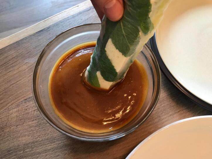 A fresh roll being dipped in peanut dipping sauce.