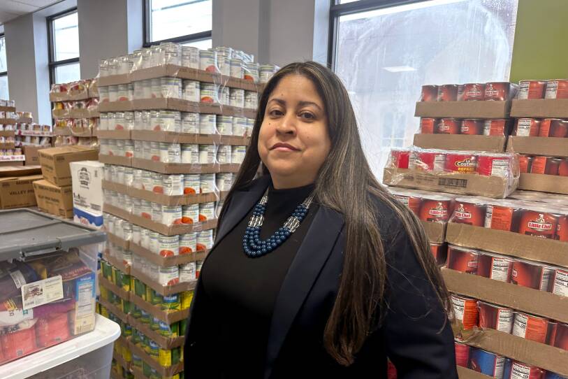 A woman stands in front of several tall stacks of canned goods.