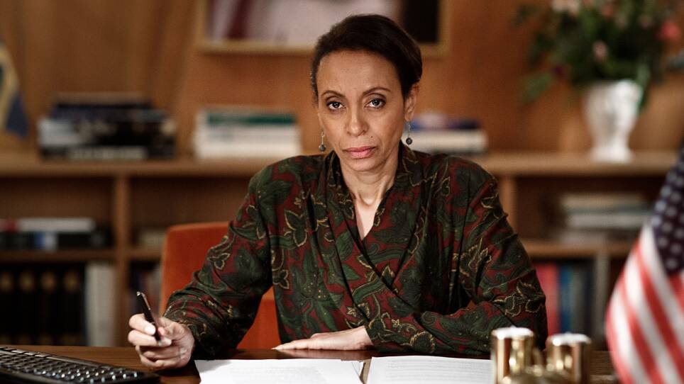 A serious woman looks into the camera. She looks into the camera, paused in the middle of signing a paper.