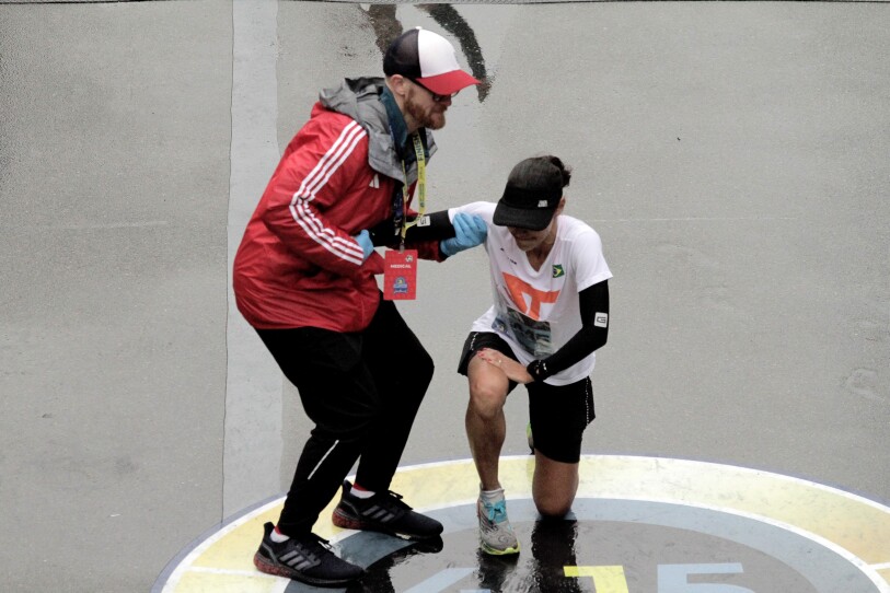 A man with a lanyard helps a runner stand up from a one-knee kneel.