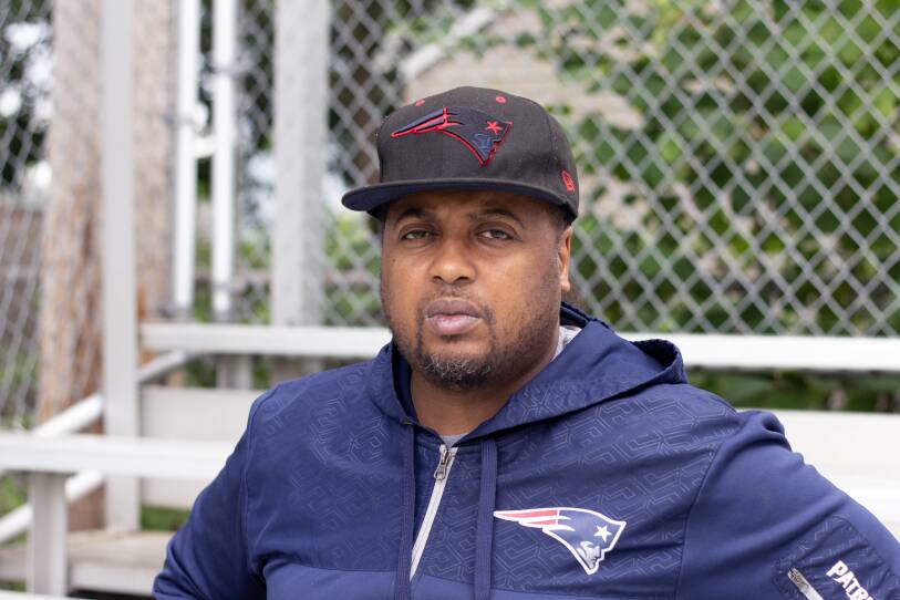 A man with a pensive and sad expression sits on bleachers at a park.