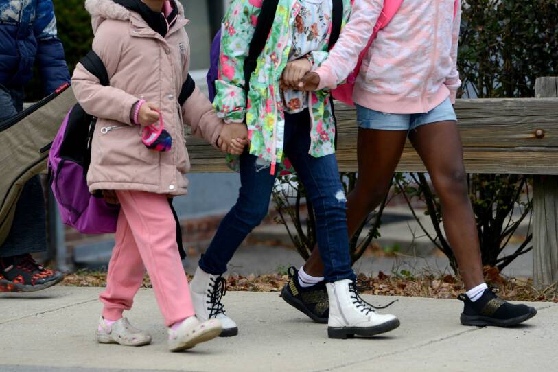 Three children hold hands as they walk along a sidewalk.