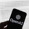 The OpenAI logo is seen on a mobile phone in front of a computer screen displaying output from ChatGPT on March 21, in Boston. A group of prominent computer scientists and other tech industry notables are calling for a 6-month pause to consider the risks of powerful artificial intelligence technology.
