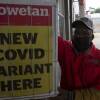 A gas station attendant stands next to a newspaper headline in Pretoria, South Africa, on Saturday. The new omicron variant has spread from South Africa to parts of Europe, and as far as Hong Kong.