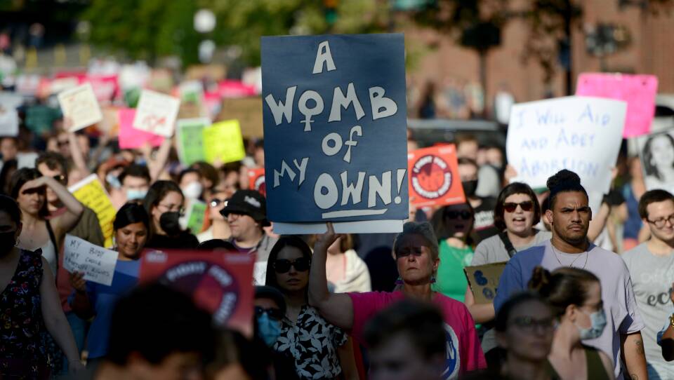 Hundreds of demonstrators march down a street holding signs about reproductive rights.
