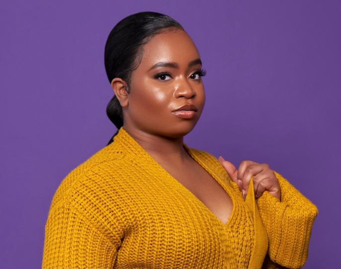 A woman wearing a mustard yellow sweater looking directly into camera