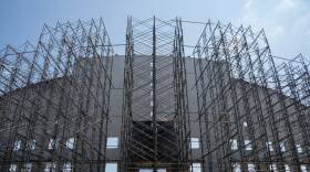 Metal scaffolding covers the front of a white facade of a stadium.