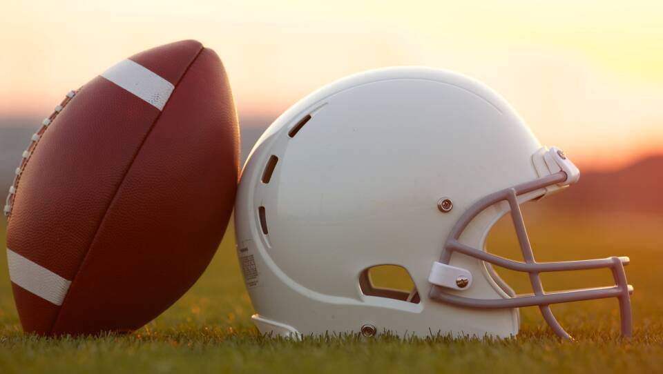 Football and Helmet on the Field at Sunset