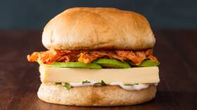 Kaiser roll topped with cilantro mayonnaise, baked egg, slices of avocado, and kimchi