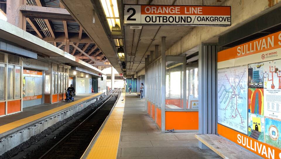 A person in a wheelchair waits on one side of a train platform, while two people stand on the other side of the tracks.