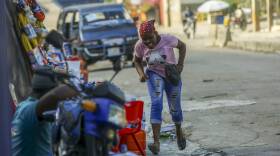 A woman on a city street, running toward the curb and ducking her head.