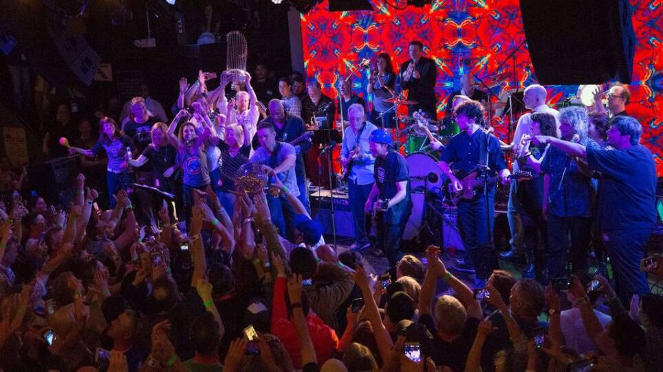 A band on stage and a crowd of fans at a music venue.
