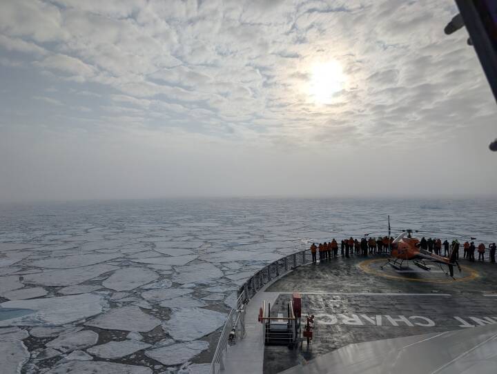 A sea of floating ice is seen over the bow of a large ship.