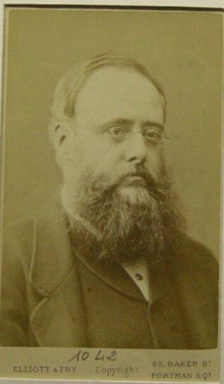 A Photograph of Wilkie Collins – he wears small glasses and a thick beard.
