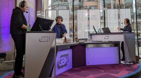 Three people sit at a desk at the Boston Public Library for a live interview