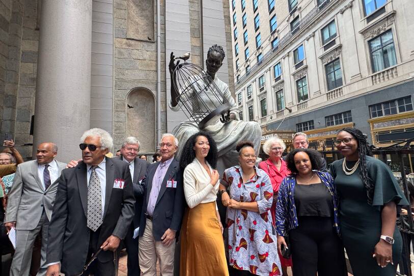 About 10 people pose with a larger-than-life statue of a Black woman in downtown Boston. They're grinning widely for the camera.