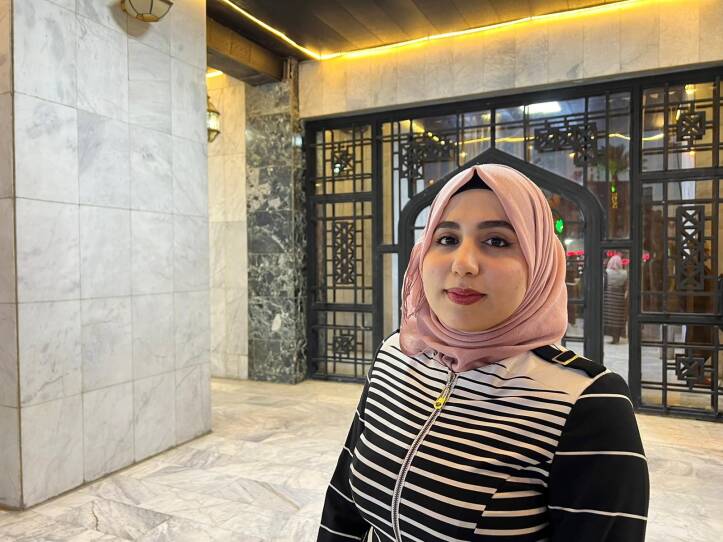 A woman wearing a head scarf stands in the ornate, marble-tiled lobby of a concert hall.