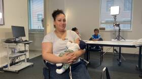 A woman sits with her baby and two children play in the background